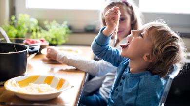 
		Zwei Kinder sitzen am Esstisch und essen Nudeln ohne Soße
	